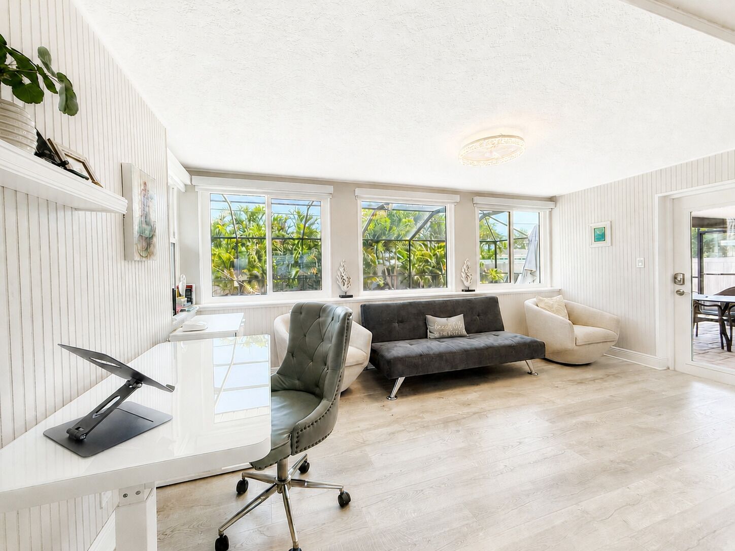 A modern living room with a white wall, a grey sofa, a white armchair, and a desk with a chair.