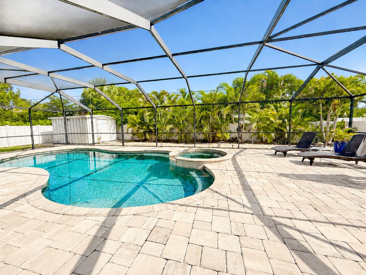 Ein Swimmingpool mit Sonnensegel, umgeben von Liegestühlen und Palmen.