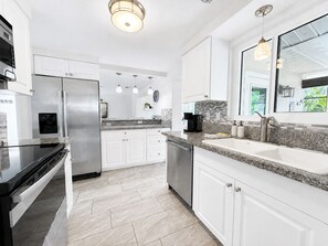A modern kitchen with stainless steel appliances, white cabinetry, and a herringbone tile backsplash. - Pool & Hot Tub near Siesta Key Beach (Sarasota)