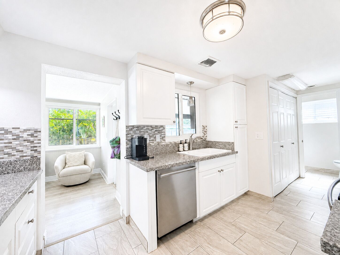 A modern kitchen with white cabinetry, a stainless steel dishwasher, and a patterned backsplash.