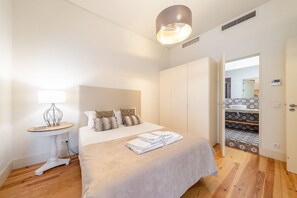 Une chambre d’hôtel avec un lit, une table de chevet, une lampe, une armoire et une salle de bain visible à travers une porte ouverte.
