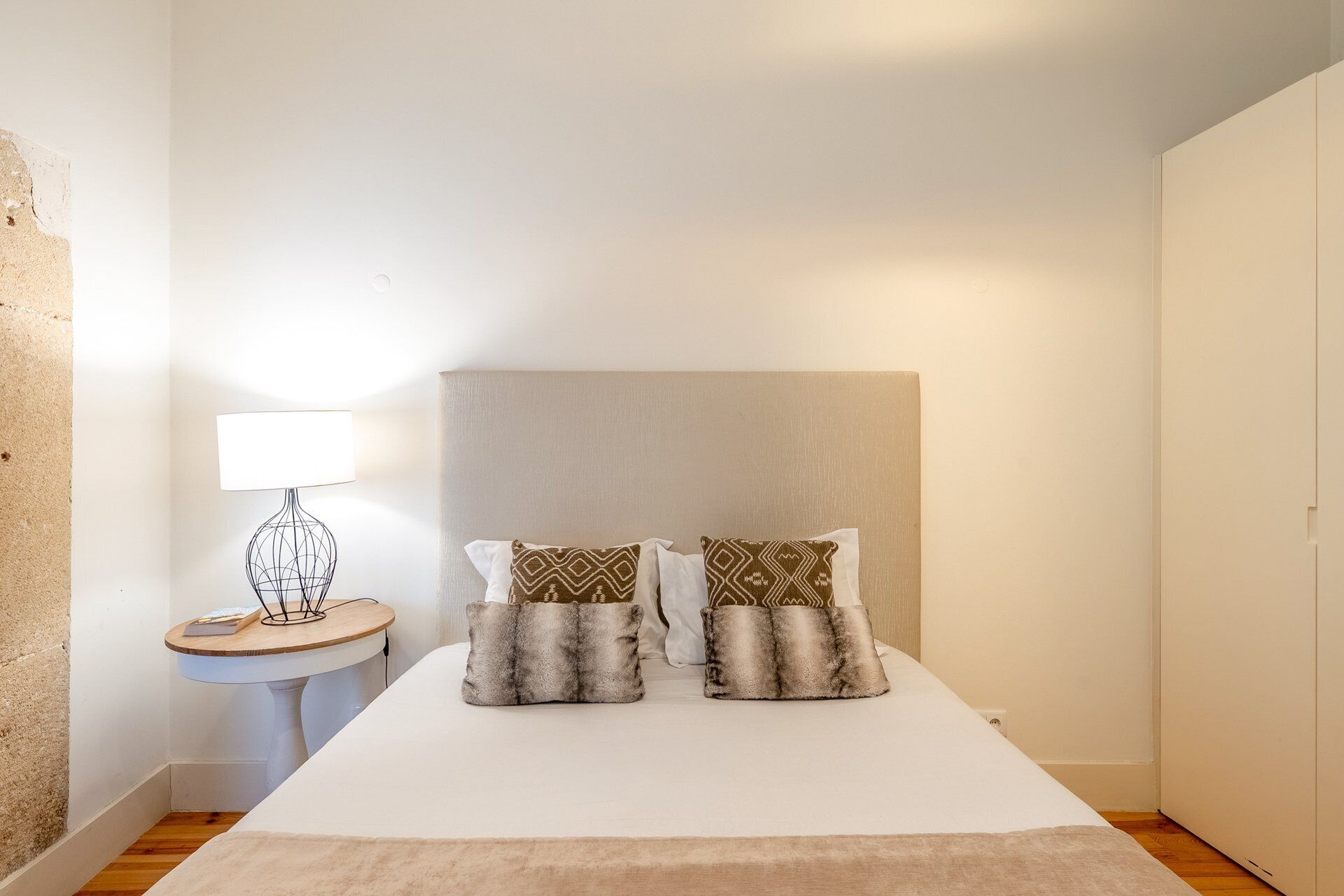 A hotel room with a bed, a bedside table with a lamp, and a wall with a textured surface.