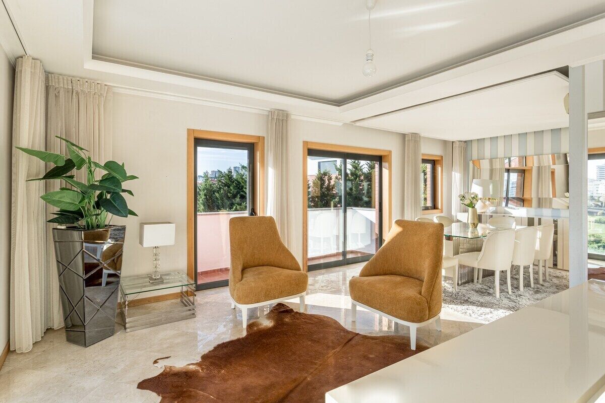 Un salón moderno con una mesa de centro de vidrio, dos sillones, una planta grande en maceta y vistas al exterior.