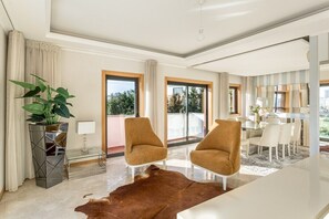 A modern living room with a glass coffee table, two armchairs, a large potted plant, and a view of the outdoors. - GuestReady - Carnaxide elegant villa with 2 pools (Carnaxide)
