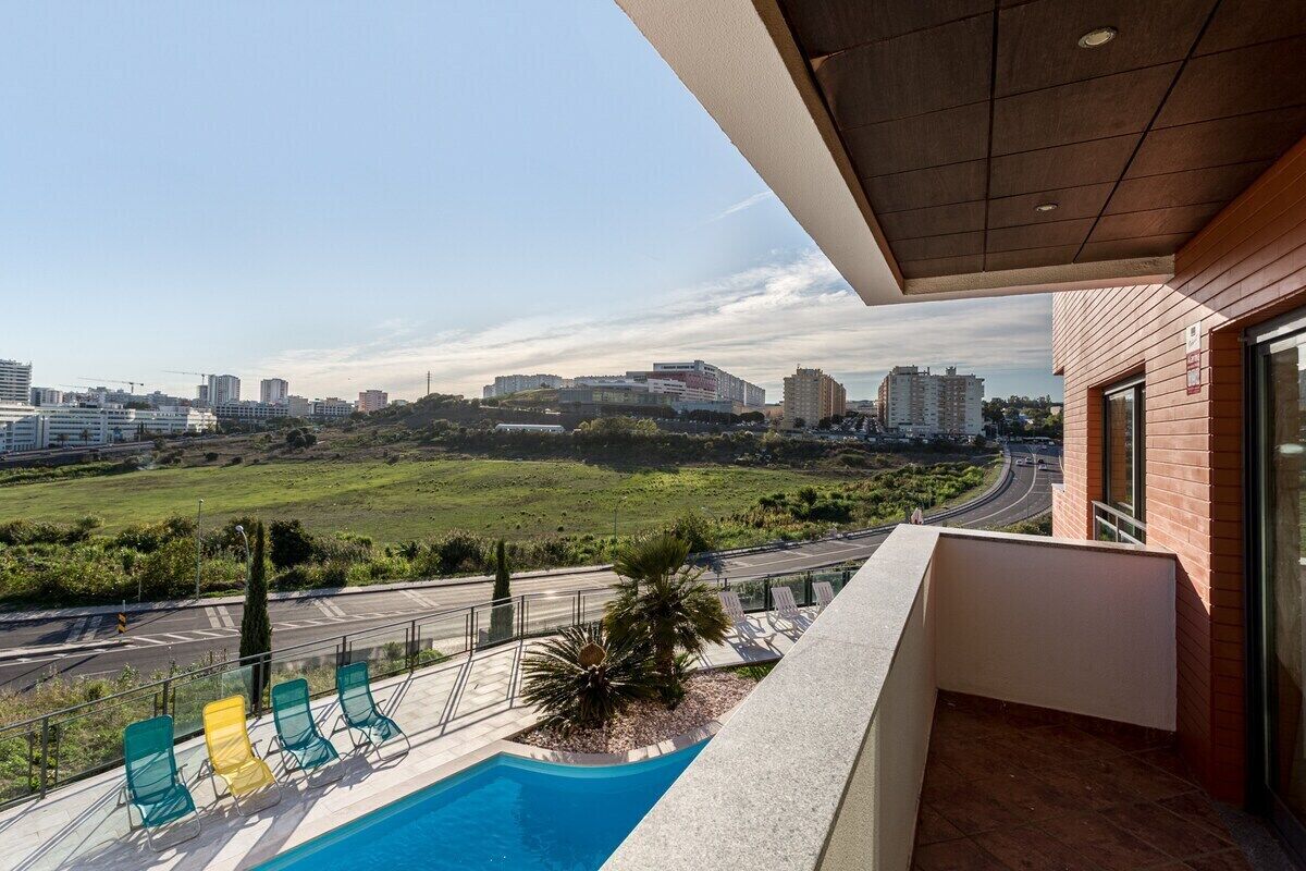 A balcony with a pool, lounge chairs, and a view of a cityscape.