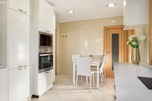 A modern kitchen with white cabinetry, a built-in oven, and a dining area with white chairs and a table. - GuestReady - Carnaxide elegant villa with 2 pools (Carnaxide)