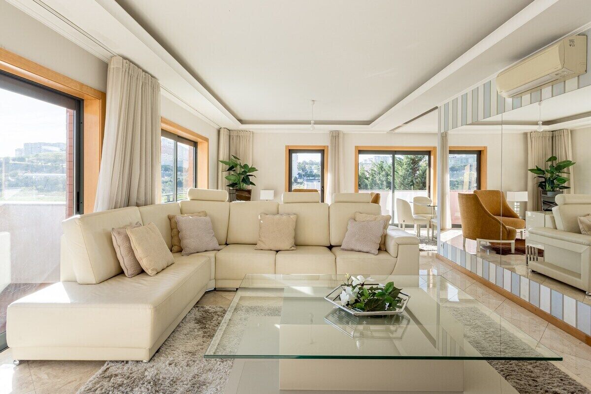 A modern living room with a sectional sofa, a glass coffee table, and a large window offering a city view.