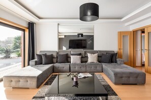 A modern living room with a sectional sofa, a coffee table, and a large window. - GuestReady - Carnaxide elegant villa with 2 pools (Carnaxide)