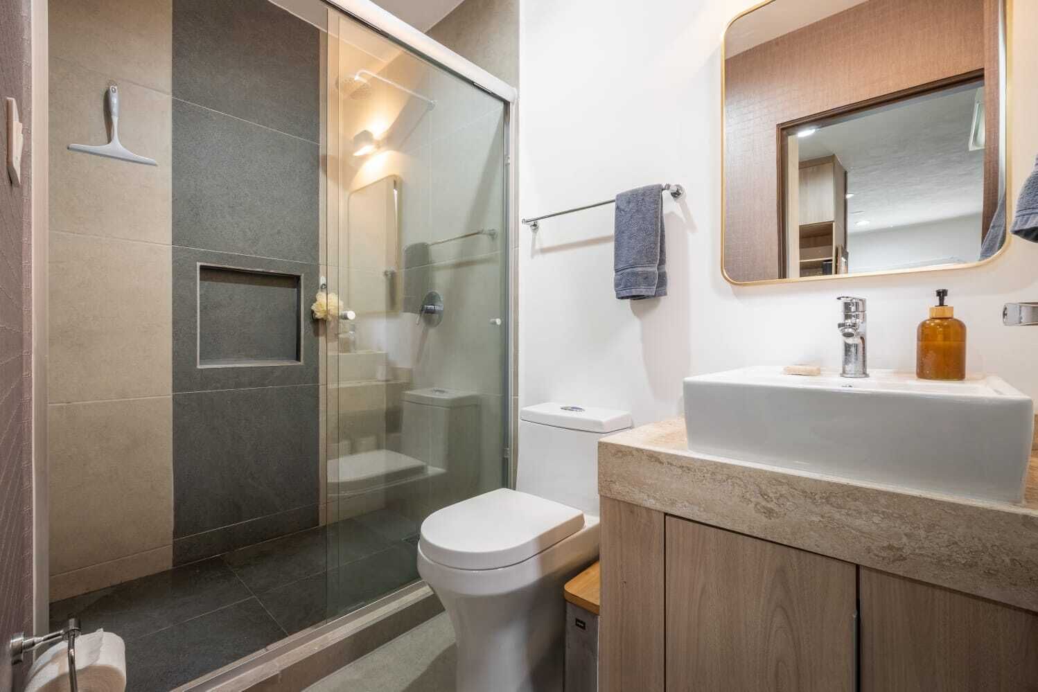 A modern bathroom with a glass-enclosed shower, a white toilet, and a wooden vanity with a mirror.