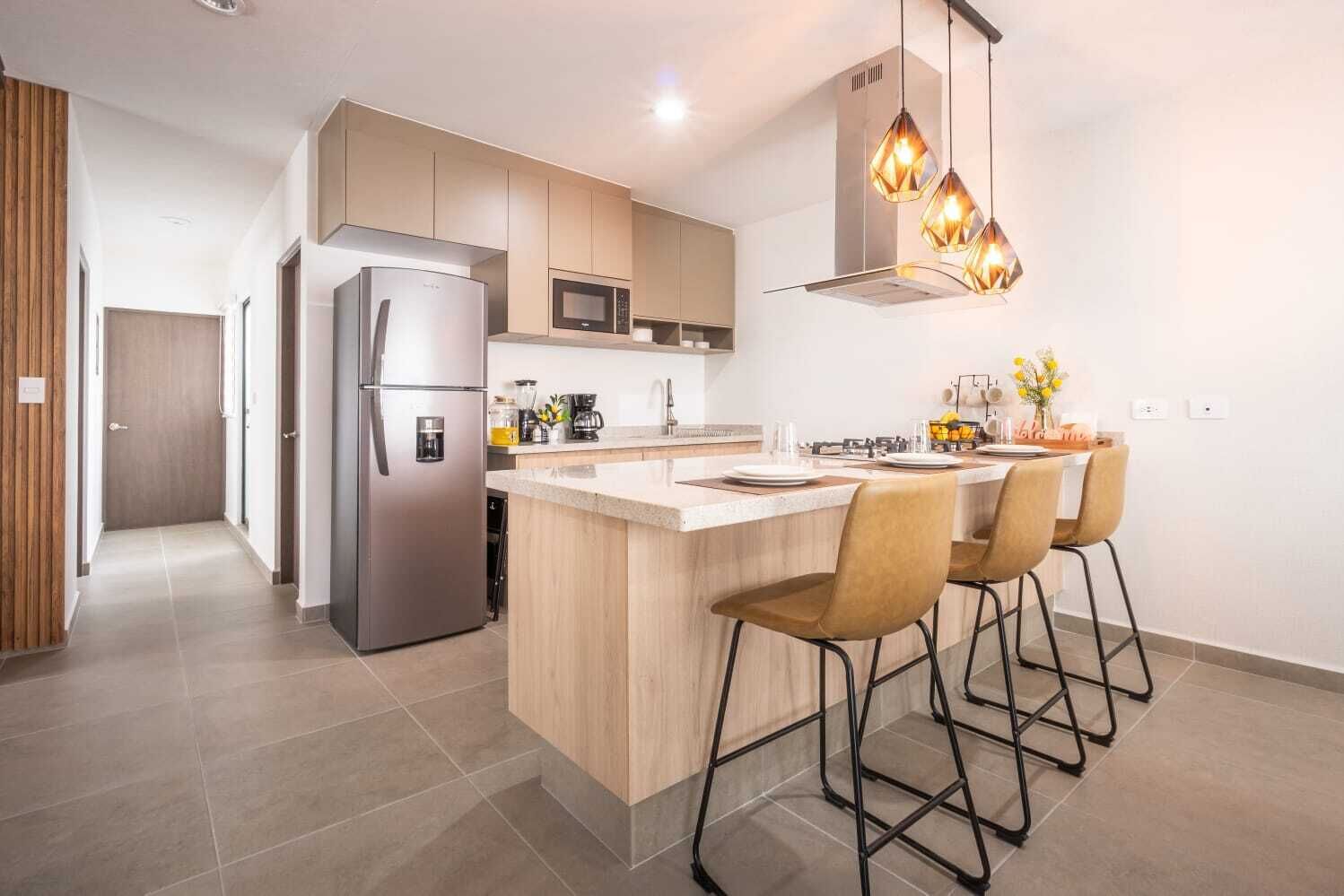 A modern kitchen with a central island, bar stools, stainless steel appliances, and pendant lighting.