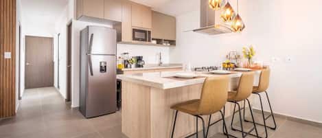 A modern kitchen with a central island, bar stools, stainless steel appliances, and pendant lighting.