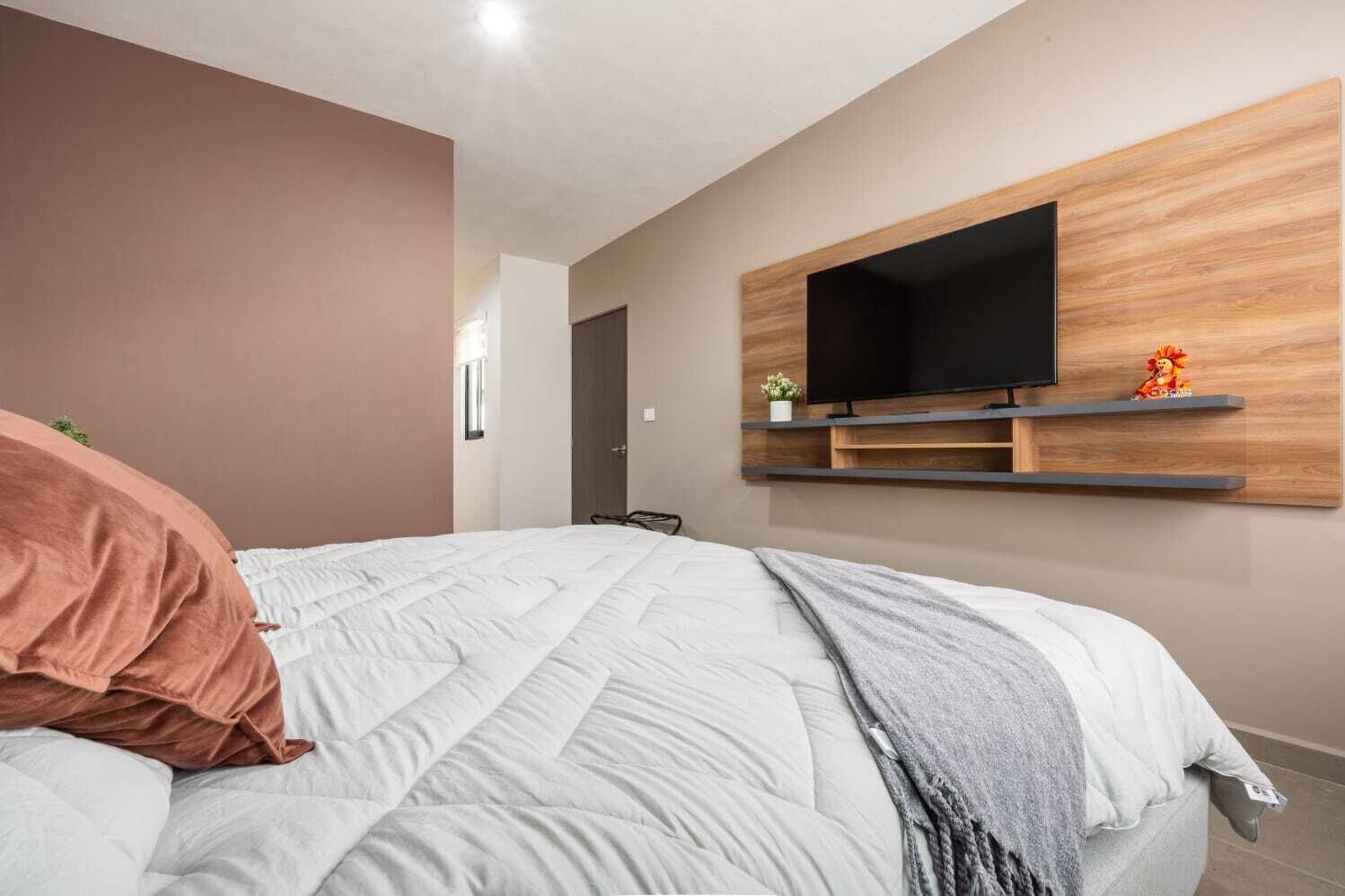 A bedroom with a bed, a mounted TV, and a door.