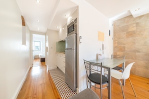 A compact kitchen with a refrigerator, microwave, and a small dining area with a table and chairs. - GuestReady - Brilliant stay near São Jorge Castle (Lisbon)