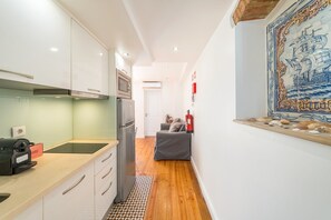 Ein schmaler Flur mit einer Küchenzeile an einer Seite, einer Sitzecke inklusive Sofa und einem Feuerlöscher an der Wand, sowie einem dekorativen Kachelbild an der gegenüberliegenden Wand.