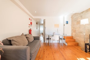 A modern living room with a grey sofa, wooden flooring, a dining area with chairs, and a staircase. - GuestReady - Brilliant stay near São Jorge Castle (Lisbon)