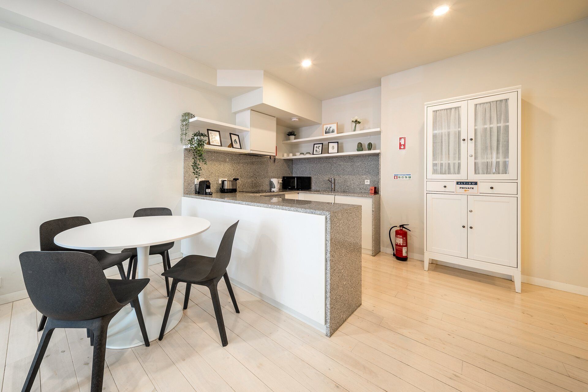 Une cuisine moderne avec un îlot central blanc, des chaises foncées et un meuble blanc doté d’une porte en verre.