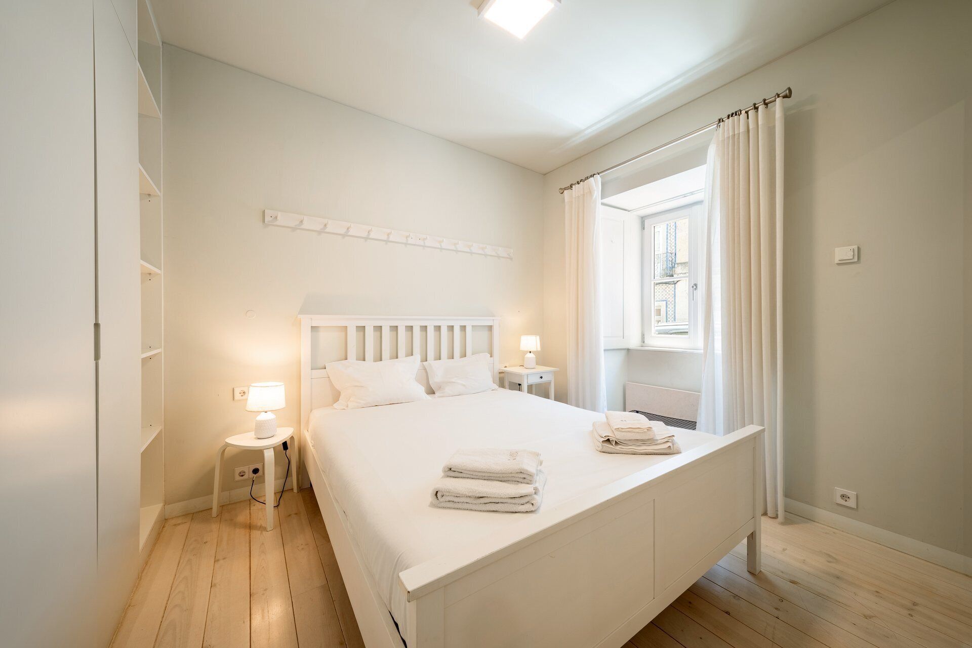 Ein Schlafzimmer mit einem Bett, Nachttischen, einem Fenster mit Vorhängen und einem an der Wand befestigten Regal.
