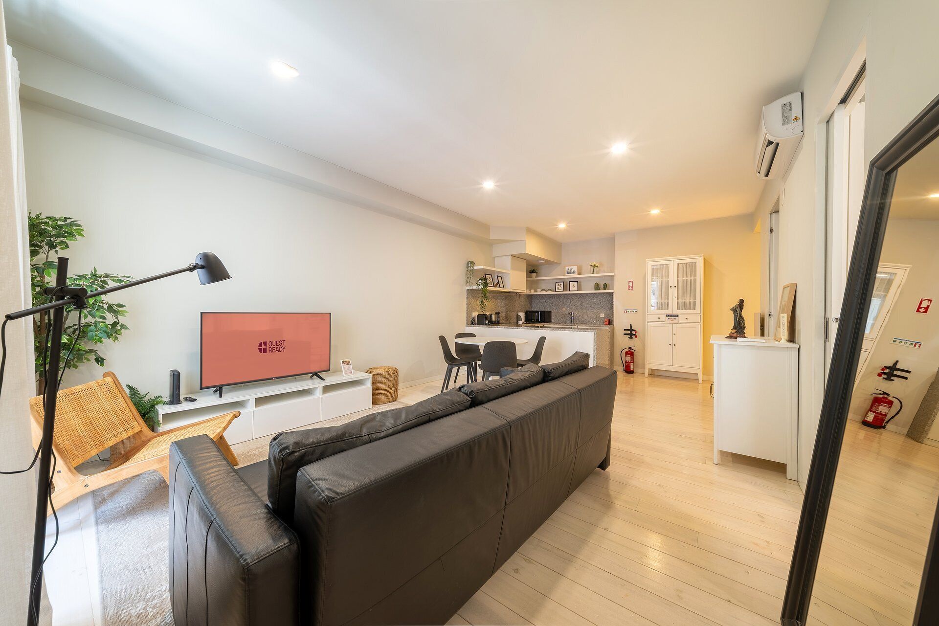 Een moderne woonkamer met een zwarte bank, een televisie en een eethoek met een tafel en stoelen.