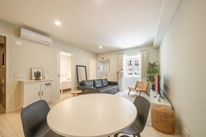Ein modernes Wohnzimmer mit einem weißen Esstisch, einem grauen Sofa und einem kleinen Beistelltisch.