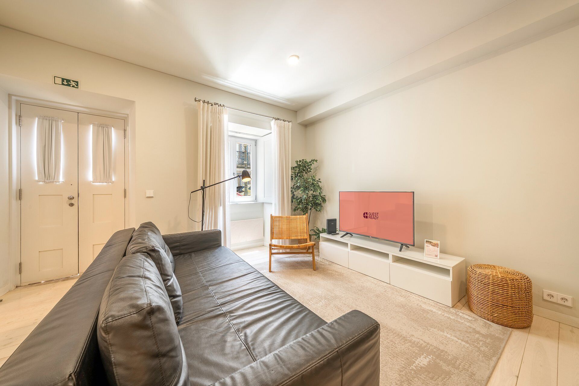 A modern living room with a leather sofa, a television, a plant, and a wicker basket.