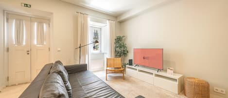 A modern living room with a leather sofa, a television, a plant, and a wicker basket.