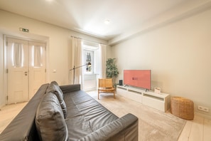 A modern living room with a leather sofa, a television, a plant, and a wicker basket. - GuestReady - Bold escape near Jardim da Estrela (Lisbon)