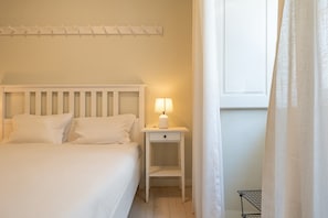 A bed with white bedding, a bedside table with a lamp, and a window with curtains. - GuestReady - Bold escape near Jardim da Estrela (Lisbon)