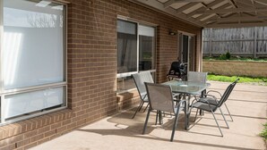 Een terras met een glazen tafel en stoelen, een barbecue en een bakstenen muur.