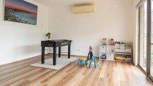 Een kamer met een houten vloer, een zwarte tafel, een klein krukje, een speelstructuur en een boekenkast met kinderspeelgoed.