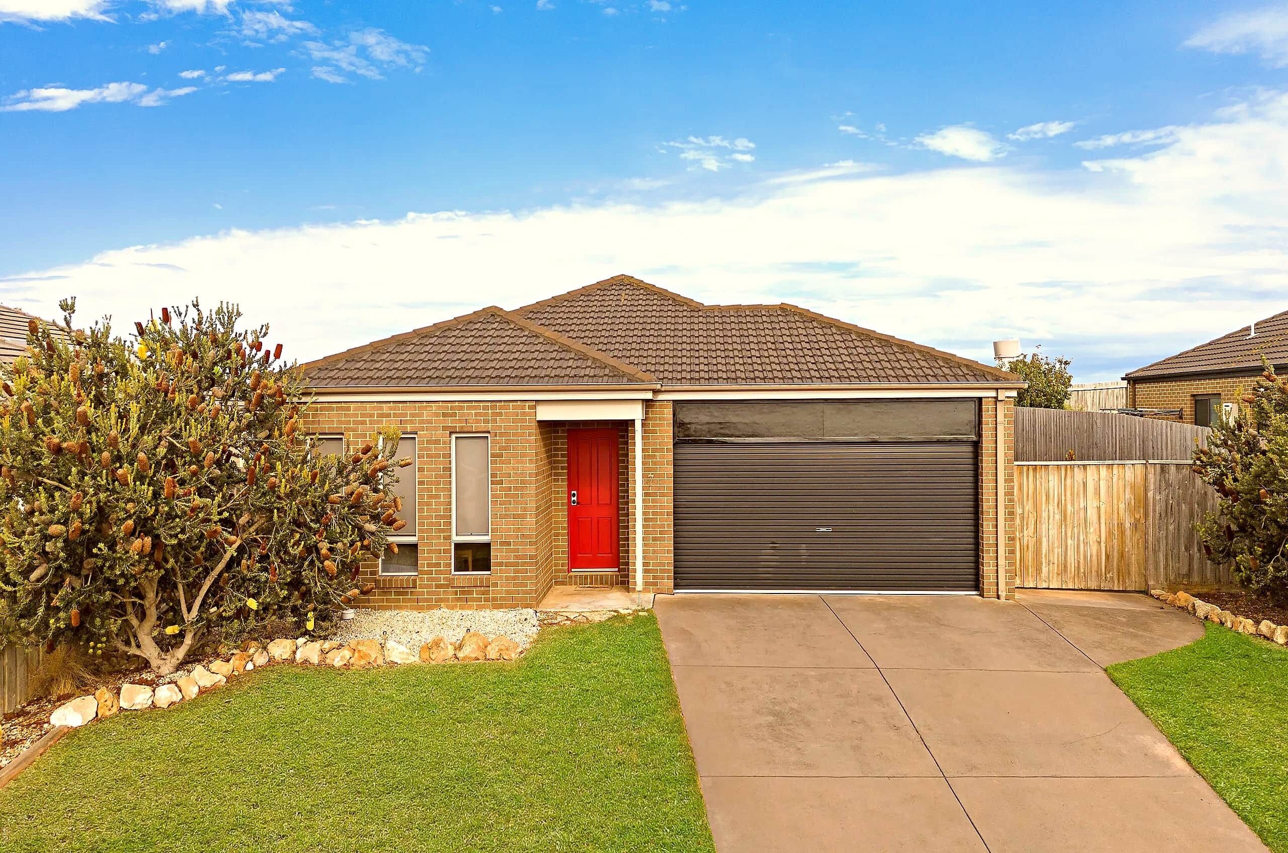 A residential house with a red door, a garage, and a well-maintained lawn.