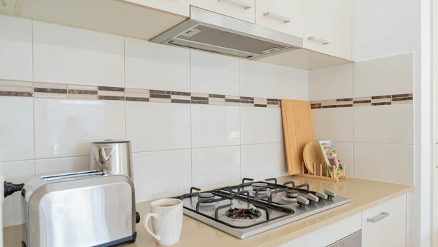 Een keuken met witte kasten, een gasfornuis, een broodrooster en een koffiezetapparaat.
