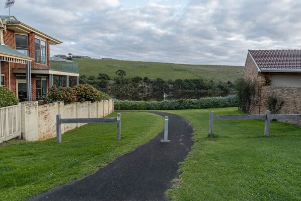 A pathway leading to a residential area with a house on the left and a hill in the background.