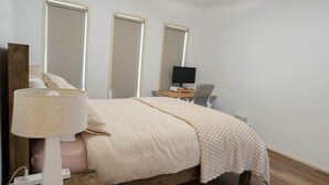 Een slaapkamer met een bed, bedlampje en een bureau met een computer.