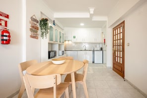 Una cocina con armarios blancos, un microondas y un lavabo. Hay un extintor de incendios en la pared y una puerta con panel de vidrio.