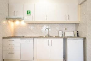 Una cocina moderna con muebles blancos, un lavamanos de acero inoxidable, una cafetera y un tostador.