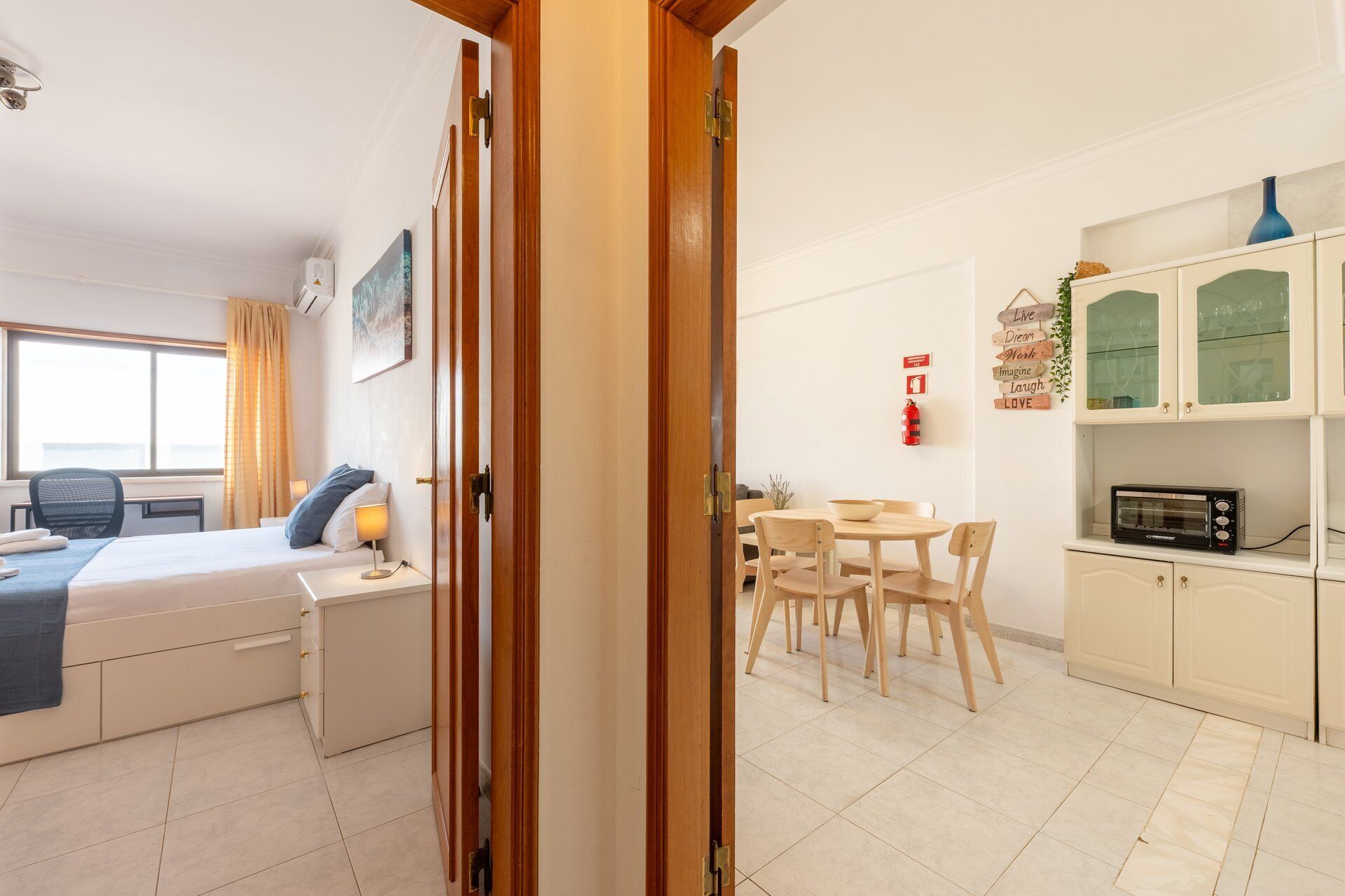 Habitación de hotel con cama, mesita de noche, lámpara, ventana y vista al comedor.