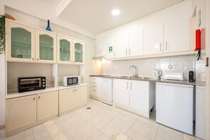 A modern kitchen with white cabinets, a microwave, a toaster, and a sink. - GuestReady - Deluxe home with terrace in Caparica (Almada)