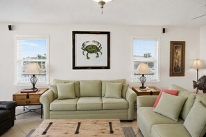 A living room with a green sofa, two side tables with lamps, a framed crab artwork, and a wooden coffee table. - Seascape St. George Island (Saint George Island)