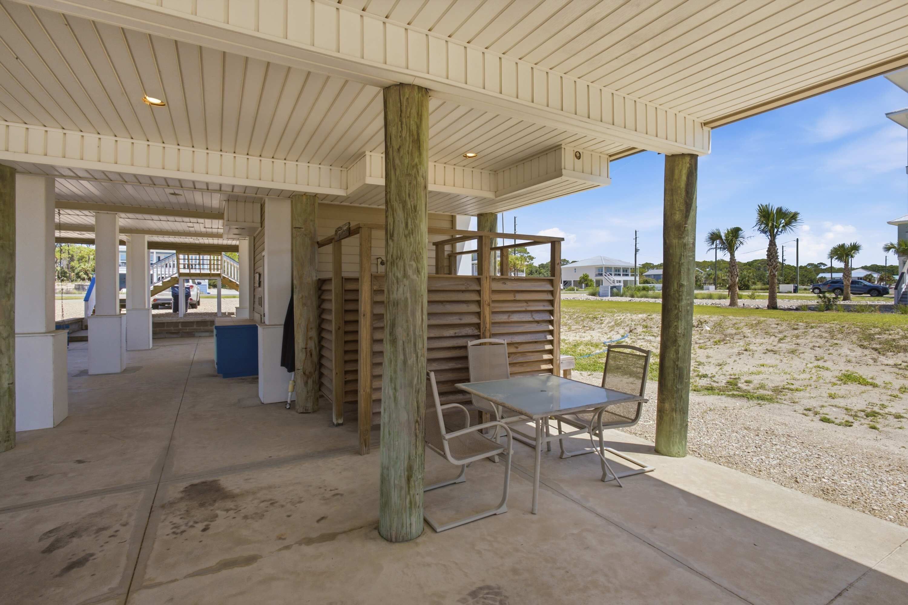 Un espace extérieur abrité, doté d’un sol en béton, de piliers en bois et d’une table avec des chaises.