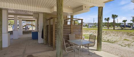 Un espace extérieur abrité, doté d’un sol en béton, de piliers en bois et d’une table avec des chaises.