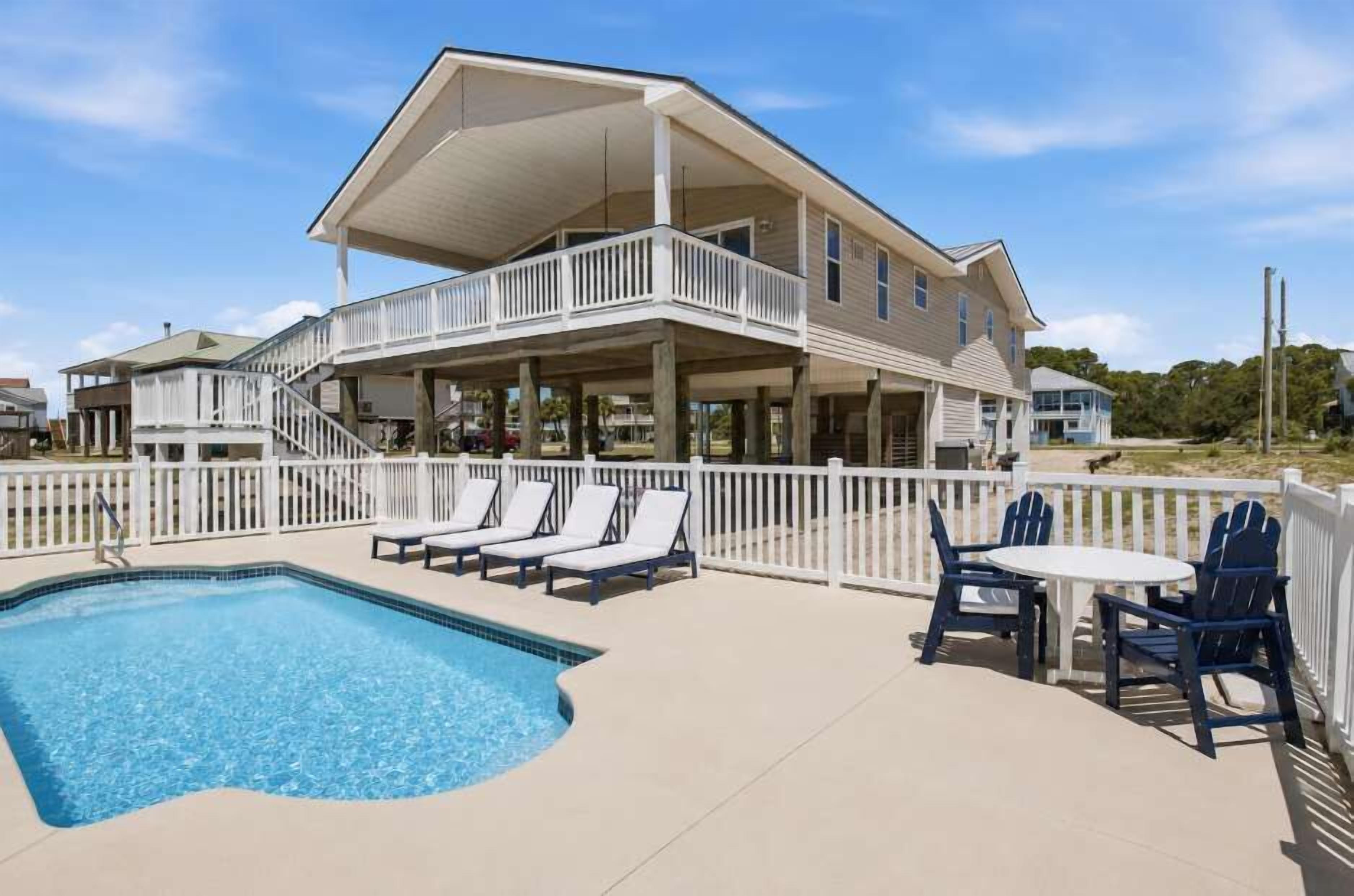 A two-story building with a pool, outdoor seating, and a white fence.