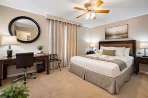 A hotel room with a bed, desk, chair, and a ceiling fan.