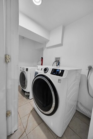 A laundry room with a front-loading washing machine and dryer, a fire extinguisher, and a water heater.