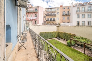 Ein Balkon mit Blick auf benachbarte Gebäude, eine kleine Gartenanlage mit Rasen und Sitzgelegenheiten sowie ein Metallgeländer.