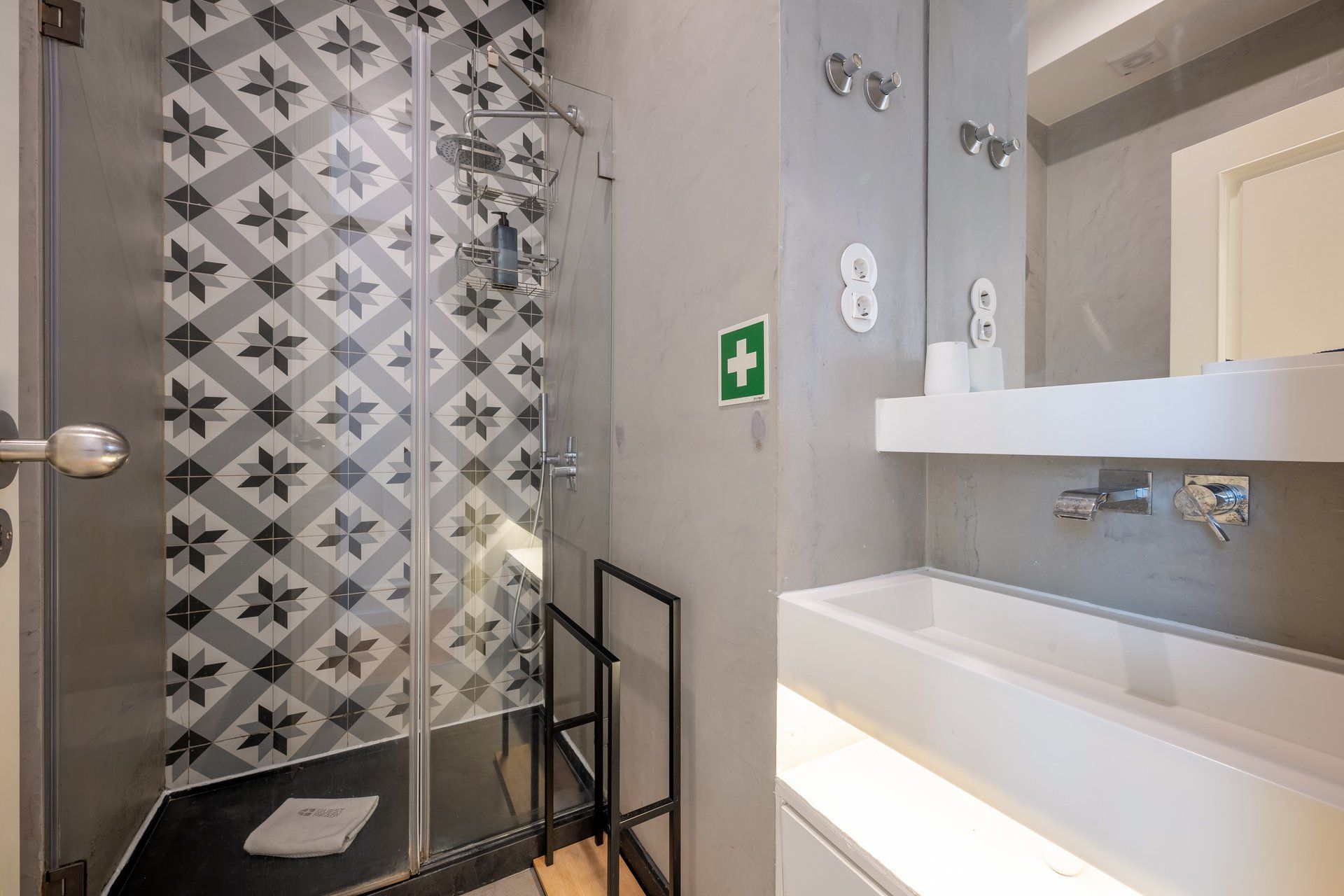 Une salle de bain avec une douche, un lavabo et des toilettes. Un panneau vert indiquant la sortie de secours est fixé au mur.