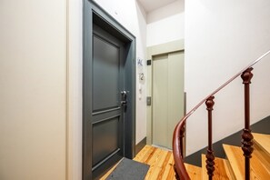 A hallway with a dark door, a wooden staircase with a handrail, and a light-colored wall. - GuestReady - Wonderful 2BR flat in the city centre (Lisbon)