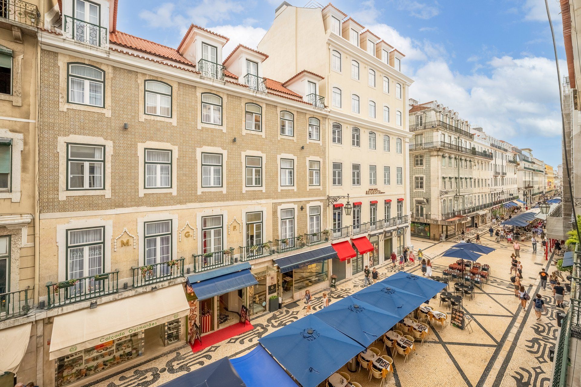 A street view with buildings, outdoor seating, and a tiled pavement.