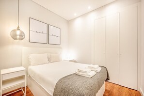 A bedroom with a bed, bedside table, wall art, and a wardrobe. - GuestReady - Lemon House with Private Garden (Lisbon)