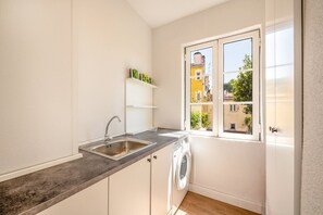Eine kompakte Küche mit Spüle, Waschmaschine und einem Fenster mit Blick auf Gebäude.