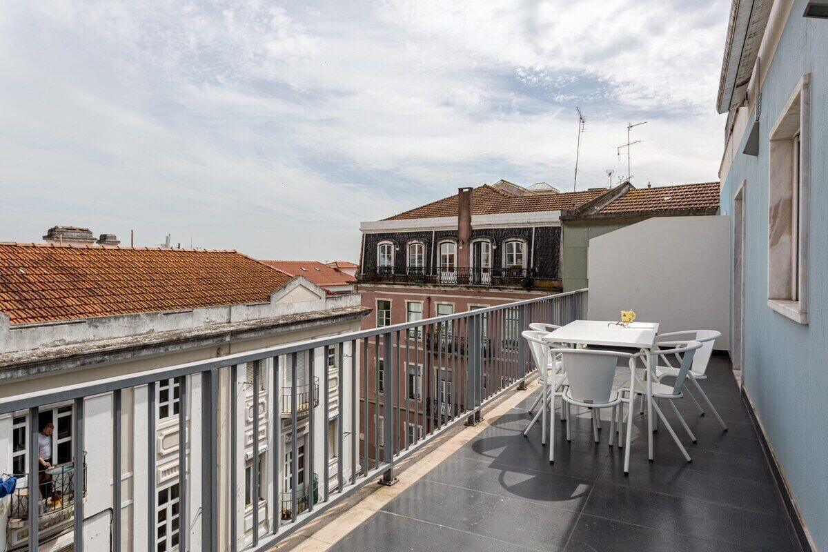 A balcony with a table and chairs, overlooking a cityscape with buildings and a clear sky.
